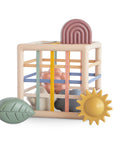 The mushie Elastic Shape Sorter is a pastel toy cube for tactile play and fine motor skills.