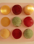 A top-down view of the Mushie Baby Food Freezer Tray, a BPA-free pink silicone tray with nine round frozen treats in yellow, red, and green arranged in a 3x3 grid—perfect for storing baby food.