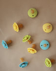 Eight FRIGG Rope Natural Rubber Pacifiers by Mushie in green, yellow, and blue are arranged on a beige background, shown from front and back views—essential baby items featuring natural rubber latex nipples. Available in 2-packs.