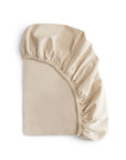 The mushie Stretchy MINI Crib Sheet in beige, made from breathable organic cotton, is shown partially folded to reveal its elasticized edge against a white background.