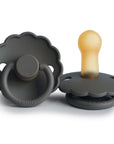 Two dark gray FRIGG Daisy Natural Rubber Pacifiers with scalloped edges—one upright displaying the latex nipple, the other flat showing the ring and base—both embossed with "FRIGG." Sold as a 2-Pack Limited Edition.