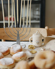 A menorah, donuts, chocolate coins, and a Mushie Silicone Training Cup + Straw on a Hanukkah table.