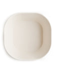 A top view of the mushie Square Dinnerware Bowl, featuring a plain off-white, square shape with rounded corners and an embossed "mushie" logo in the center. This BPA-free baby bowl is set against a white background.