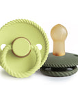 The Mushie FRIGG Rope Natural Rubber Pacifier 2-Pack features pacifiers with round, rope-textured edges and ring handles in light green and olive green; one stands upright while the other lies flat.