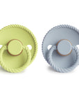 The FRIGG Rope Natural Rubber Pacifier 2-Pack by Mushie includes one light green and one light blue pacifier, each with a rope-textured edge, natural rubber latex nipple, knob, ring handle, and embossed branding—perfect baby essentials.