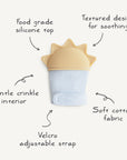 The mushie Sun Teething Mitten features a yellow, sun-shaped silicone top, soft blue cotton fabric, Velcro strap, gentle crinkle interior, and soothing textures for babies. Labeled features highlight its thoughtful design.