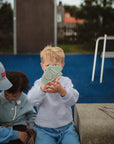 A child holds a mushie Silicone Sensory Toy while sitting with friends at the playground.