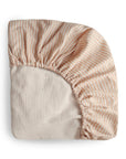 The mushie Extra Soft Muslin Crib Sheet features beige and white stripes with elastic edges, crafted from breathable baby bedding, and is shown folded on a white background.