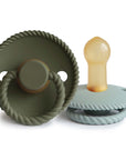 The Mushie FRIGG Rope Natural Rubber Pacifier 2-Pack features two pacifiers—one with an olive green looped handle and one in pale blue with a beige natural rubber latex nipple, both styled with a rope-like textured edge. Essential for any nursery.