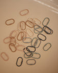 A scattered arrangement of mushie’s Chain Link Rings in beige, pink, green, and gray rests on a light peach surface with soft lighting—ideal for promoting fine motor skills.