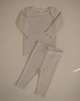 The mushie Two Piece Set features a light beige ribbed long sleeve shirt and pants made from breathable, soft fabric, perfect for children. Shown laid flat on a neutral background.
