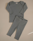 The mushie Two Piece Set features a breathable, soft ribbed long sleeve shirt and pants in muted blue-gray, laid flat on a beige surface—ideal for comfort and style.