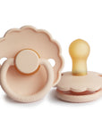 Two soft Pink Cream FRIGG Daisy Natural Rubber Pacifiers (Limited Edition) with scalloped edges; one stands showing the nipple, the other lies flat displaying the handle and FRIGG branding on the base.