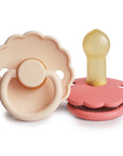 The FRIGG Daisy Natural Rubber Pacifier 2-Pack features two pink, daisy-shaped pacifiers: one front-facing showing the FRIGG brand, and another side view displaying the natural rubber nipple and pink shield.