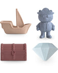 The mushie Pirate Mold Free Bath Play Set features four non-toxic silicone toys—a beige pirate ship, blue pirate bear, mauve treasure chest, and light blue diamond—for safe, mold-free bath time fun.
