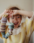 Smiling child with mushie Bead Lacing Toy Set, stacking rings for motor skill development.