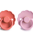The FRIGG Daisy Natural Rubber Pacifier 2-Pack features two daisy-shaped pacifiers—one coral red, one light lavender—with scalloped edges and round handles, shown side by side on a white background. Each has a natural rubber latex nipple.