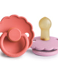 The FRIGG Daisy Natural Rubber Pacifier 2-Pack features two daisy-shaped pacifiers with scalloped edges—one in rose pink with a forward-facing ring, the other in lavender with a natural rubber latex nipple.
