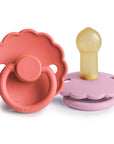 The FRIGG Daisy Natural Rubber Pacifier 2-Pack features two colorful pacifiers—one coral pink and one lavender—with scalloped, daisy-shaped edges, from the brand FRIGG.