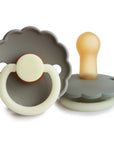 Two FRIGG Daisy Natural Rubber Pacifiers (Portobello Night) are shown—one flat with a gray scalloped shield and cream ring, the other upright highlighting the amber latex nipple and matching gray shield. Limited Edition 2-Pack.