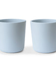 Two plain, white, cylindrical Dinnerware Cups by mushie sit side by side on a white surface with soft shadows beneath them.