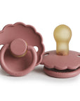 Two FRIGG Daisy Natural Rubber Pacifiers in Powder Blush are shown, featuring scalloped edges and yellowish latex nipples. One is upright, one flat, each with "FRIGG" embossed on the front. Limited Edition 2-Pack.