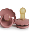 Two FRIGG Daisy Natural Rubber Pacifiers in Powder Blush—one flat to show the nipple, one upright showing the handle and FRIGG branding—feature scalloped edges. This limited edition 2-pack combines style and function.