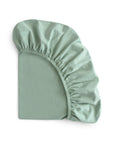 The mushie Stretchy MINI Crib Sheet in light green organic cotton is partially folded on a white background, revealing its elastic edge and soft, breathable texture.