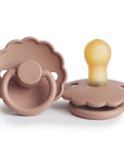Two rose gold FRIGG Daisy Natural Rubber Pacifiers (Limited Edition) feature scalloped edges, round handles, and "FRIGG" embossed on the base—one upright and one lying on its side.