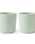 Two non-toxic, light green Dinnerware Cups by mushie are placed side by side on a white background, ideal for kids.