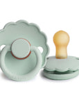 The FRIGG Daisy Natural Rubber Pacifier 2-Pack in Seafoam features two limited edition scalloped-edge pacifiers with natural rubber nipples. One stands upright, the other lies flat, both displaying the embossed FRIGG brand on the handle.