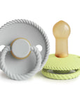 The Mushie FRIGG Rope Natural Rubber Pacifier 2-Pack is shown in gray and light yellow-green, each with a braided edge and translucent brown natural rubber latex nipple, displayed from side and front views.