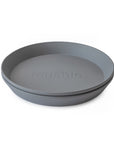 The mushie Round Dinnerware Plate is a gray plastic plate with slightly raised edges and "mushie" embossed in the center. Dishwasher safe.