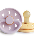The FRIGG Moon Natural Rubber Pacifier 2-Pack by FRIGG includes Soft Lilac and Daffodil pacifiers with round handles, ventilation holes, and natural rubber nipples—an essential set for every baby.