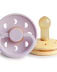The FRIGG Moon Natural Rubber Pacifier 2-Pack from FRIGG features Soft Lilac and Daffodil colors, round shields with multiple ventilation holes, and natural rubber nipples for comfort.