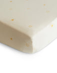 A close-up of the mushie Stretchy MINI Crib Sheet in cream, crafted from organic cotton with breathable fabric and evenly spaced simple yellow sun designs.