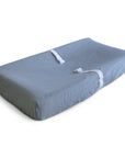 The mushie Extra Soft Muslin Changing Pad Cover is shown on a gray, contoured pad with two white safety straps, set against a white background.