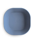 The Square Dinnerware Bowl by mushie is a blue, BPA-free silicone baby bowl with rounded corners and the brand embossed in the center. Shown from above on a white background, it’s perfect for plastic dinnerware sets.