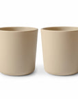 Two beige, cylindrical ceramic plant pots sit side by side on a plain white background, complementing mushie Dinnerware Cups in a modern home.