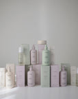 A selection of mushie Fragrance Free Baby Body Lotion in soft pastel pink, green, and cream bottles, pumps, and boxes is arranged in a pyramid on a white surface.