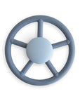 The mushie Suction Spinner Toy in Wheel color, made from food-grade silicone and shaped like a steering wheel with "mushie" at the center, provides a gentle sensory experience and is shown from above on a white background.