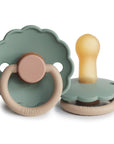 The FRIGG Daisy Natural Rubber Pacifier 2-Pack | Limited Edition features two silicone pacifiers in muted green and beige with scalloped edges. One stands upright, the other on its side, both displaying the FRIGG brand—ideal for soothing babies.