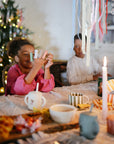 Smiling kids play with mushie Silicone Animal Finger Puppets at a table with treats and candles.
