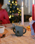 Mushie Silicone Training Cup + Straw with Christmas tree, on table with candles and child behind.