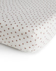 The mushie Extra Soft Muslin Crib Sheet features a white background with small, evenly spaced brown floral patterns, providing breathable and cozy bedding for your baby’s crib.