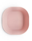 A light pink, square BPA-free silicone bowl from mushie's Square Dinnerware Bowls collection features rounded edges and an embossed brand name in the center, shown from above on a white background.