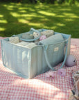Light blue organizer bag with rolled towels and mushie Silicone Pacifier Case on a picnic blanket.