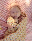 Baby in a pink hat with mushie Linen Pacifier Clip 2-Pack, sleeping on pink checks.