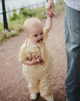 A toddler in yellow walks outside, sucking a FRIGG Daisy Natural Rubber Pacifier.