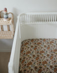 White crib with mushie Extra Soft Muslin Crib Sheet beside a shelf with stacking toy and basket.